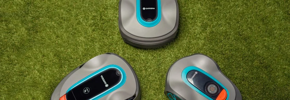 Drei Rasenroboter auf grünem Rasen.